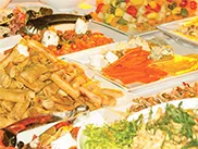 Bankets brīvā dabā ar baltām teltīm, salātu galdu un dekoratīvu gaismojumu